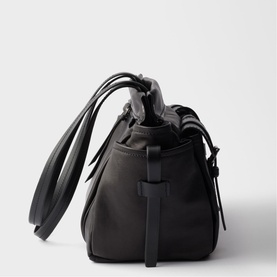 Black structured bucket bag with drawstring top, dual top handles, adjustable side strap, and black hardware, side view