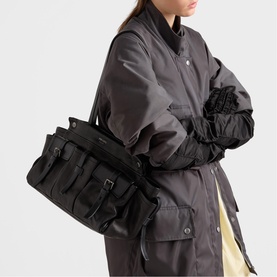 Model carrying large black leather holdall with buckle detail and multiple pockets, styled with dark grey bomber jacket