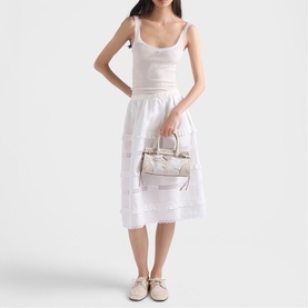 Model carrying Prada Accessories white structured top-handle bag with gold hardware, styled with a white midi dress and beige loafers.