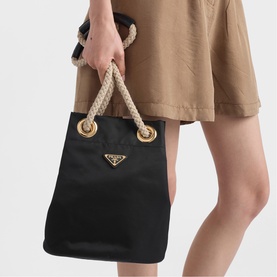 Model carrying Prada Accessories black nylon tote bag with rope handles and gold-tone triangle logo hardware