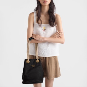 Model carrying Prada Accessories black tote bag with rope handles and gold-tone triangle logo, styled with white tank top and tan mini skirt