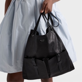 Model carrying Prada Accessories black leather tote bag with dual top handles, silver-tone hardware, and front patch pockets.