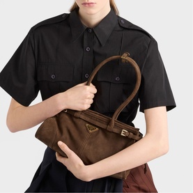 Model carrying Prada Accessories brown suede tote bag with gold hardware and short top handles, styled with black shirt dress