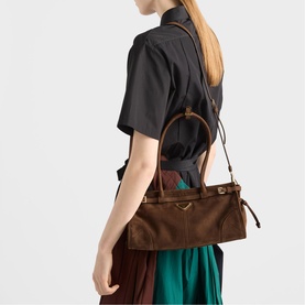 Model carrying Prada Accessories brown leather tote bag with gold hardware and top handles, styled with black shirt and teal skirt