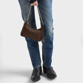 Model carrying a brown shoulder bag with gold chain strap, styled with blue jeans and black leather shoes