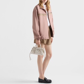 Model carrying a small white leather handbag with gold hardware and top handles, styled with a pink jacket, khaki shorts and black loafers