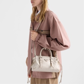 Model carrying a small white leather structured top-handle bag with silver hardware and detachable shoulder strap, styled with a pink oversized