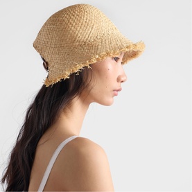 Model with Prada Accessories neutral raffia bucket hat with frayed brim detail, worn with white strappy top