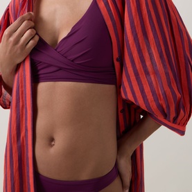 Model wearing Sea Level Essentials Sporty Bikini Bottoms in Claret, mid-rise with high-cut leg, styled with a red striped robe and matching bikini