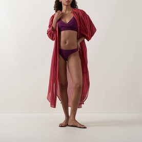 Model wearing Sea Level Essentials Sporty Bikini Bottoms in Claret, mid-rise, high-cut leg, styled with matching purple bikini top and striped kimono.