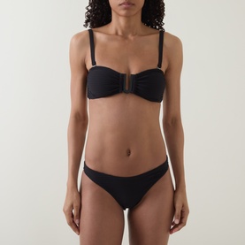Model wearing Sea Level black bikini bottom with matching black bandeau bikini top featuring ring detail at centre front.
