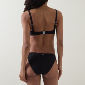 Model wearing Sea Level black bikini bottom, back view, paired with matching black bikini top with silver hardware detail.