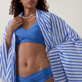 Model wearing Sea Level Essentials V-Front Bikini Bottoms in Denim Blue with matching bikini top and blue striped shirt, pearl necklace.