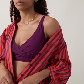 Model wearing Sea Level Essentials Cross Front Multifit Bikini Top in Claret with a red and navy striped shirt and gold chain necklace.