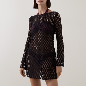 Model wearing Sea Level black crochet mesh cover-up mini dress with long sleeves, styled over a dark swimsuit.