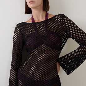 Model wearing Sea Level Black mesh cover-up with open-knit detail, styled over a dark purple bikini top with halterneck tie.