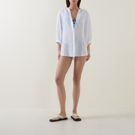 Model wearing Sea Level white cotton cover-up shirt, styled with blue swimwear and beige flat sandals