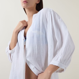 Model wearing Sea Level white cotton cover-up, open front with three-quarter sleeves, styled over a blue bikini top.