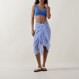 Model wearing Sea Level Vacay Striped Sarong in chambray, tied as midi wrap skirt. Styled with blue bikini top and brown sandals.