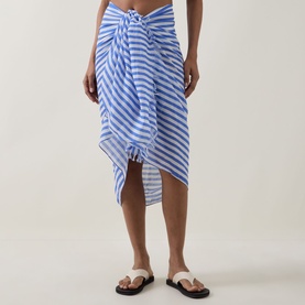Model wearing Sea Level Vacay Striped Sarong in chambray blue and white stripes, tied at waist, with black flat sandals.