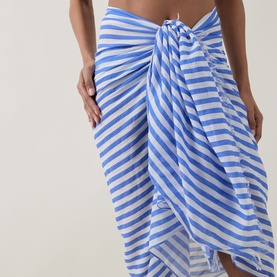 Model wearing Sea Level Vacay Striped Sarong in Chambray, tied at waist as skirt with blue and white stripes and frayed edges