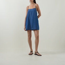Model wearing Sea Level Denim Surf Mini Shift Dress in denim, straight neckline, narrow straps, flared mini skirt, styled with flat sandals