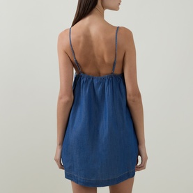 Model wearing Sea Level Denim Surf Mini Shift Dress in denim, showing low back with narrow adjustable straps and rear pleating detail.