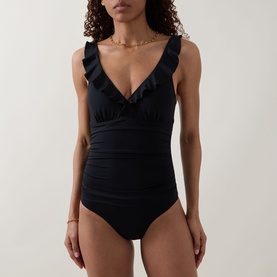 Model wearing Sea Level Essentials Edit Frill One-Piece Swimsuit in black with V-neckline, ruched front, and soft frill detailing