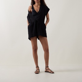 Model wearing Sea Level Essentials Edit Frill One-Piece Swimsuit in black, styled with a cover-up wrap and strappy flat sandals.