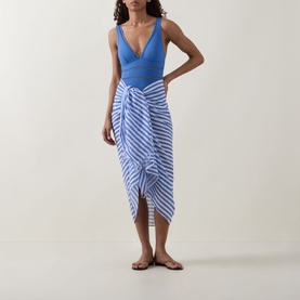 Model wearing Sea Level Essentials Edit Spliced One-Piece Swimsuit in Denim Blue with a blue and white striped sarong and tan sandals.