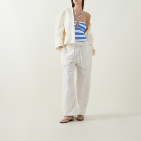 Model wearing Sea Level Denim Blue swimsuit styled with cream wide-leg trousers, oversized white jacket and tan sandals.