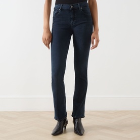 Model wearing Seven Jeans Tailorless Mid-Rise Bootcut Jeans in dark blue with split unfinished hems, styled with black ankle boots.