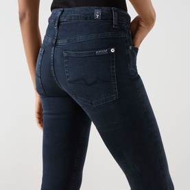 Model wearing Seven Jeans Tailorless Mid-Rise Bootcut Jeans in dark blue, showing rear five-pocket styling and logo badge detail.