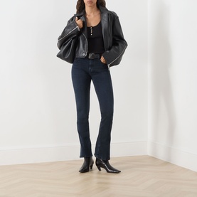 Model wearing Seven Jeans Tailorless Mid-Rise Bootcut Jeans in dark blue with split hems, styled with black leather jacket and ankle boots.