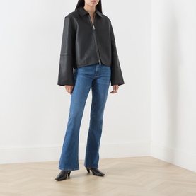 Model wearing Seven Jeans blue bootcut jeans, styled with a black leather zip-up jacket and black heeled ankle boots.