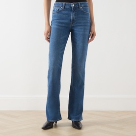 Model wearing Seven Jeans blue bootcut jeans in mid-wash denim, styled with black leather boots.