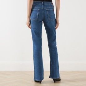 Model wearing Seven Jeans blue bootcut jeans, rear view showing back pockets and slight flare hem.