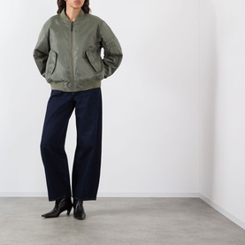 Model wearing khaki bomber jacket with zip front and flap pockets, styled with wide-leg navy trousers and black heeled boots