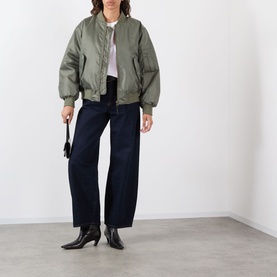 Model wearing khaki oversized bomber jacket with navy wide-leg trousers and black heeled ankle boots, carrying a small black bag