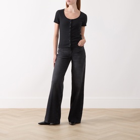 Model wearing Seven Jeans black wide leg jeans in denim, styled with a black short-sleeve scoop-neck top and black pointed flats.