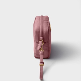 Dusty pink crossbody bag with gold-tone hardware, zip top closure, and adjustable crossbody strap, side profile view