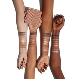 Four arms with varying skin tones showing bronze shimmer eyeshadow swatches, with a gold quilted compact held between two hands.