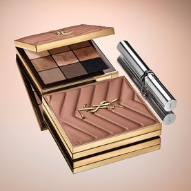 YSL eyeshadow palette in neutral nudes with quilted bronzer compact and mascara, gold packaging, displayed open on warm beige background