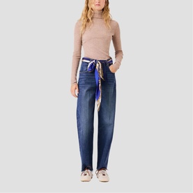 Model wearing Maje wide-leg dark blue jeans with colourful scarf belt, styled with a beige turtleneck top and white trainers.