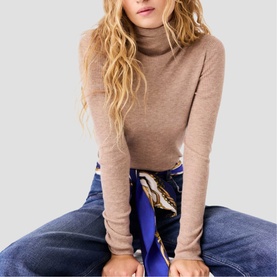 Model wearing Maje camel fine-knit turtleneck top, styled with blue jeans and a printed scarf at the waist