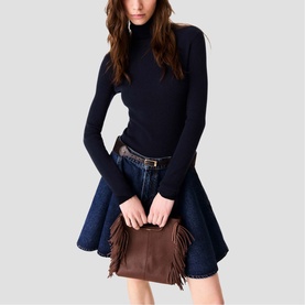 Model carrying Maje brown fringe mini bag with top handle, styled with navy turtleneck and denim skirt