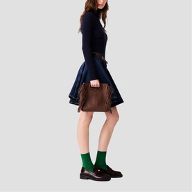 Model carrying Maje bag in brown with fringe detail and gold hardware, styled with navy dress, green socks and black loafers