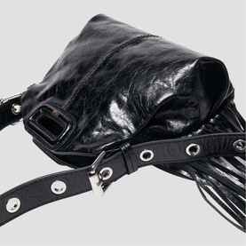 Maje black leather bag with silver hardware, eyelet-studded strap, and fringe detail, shown in close-up flat lay