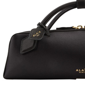 Alaia noir calf leather clutch bag, close-up showing dual top handles, branded tab, and gold-tone hardware detail