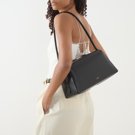 Model carrying Alaia Le Bouledogue Shoulder Bag in Noir, black leather with gold-tone hardware and tubular strap, styled with white cami and cream